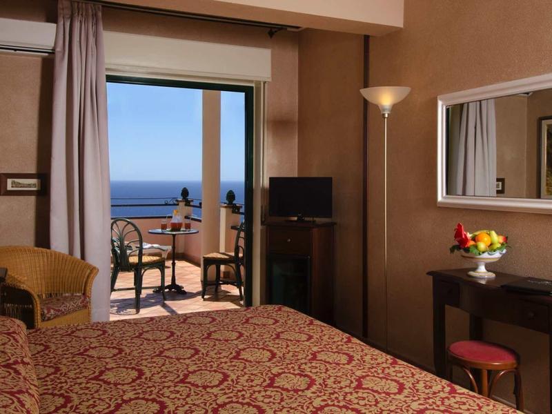 Hotelkamer met eenpersoonsbed, balkon met uitzicht op zee en eenvoudige inrichting.