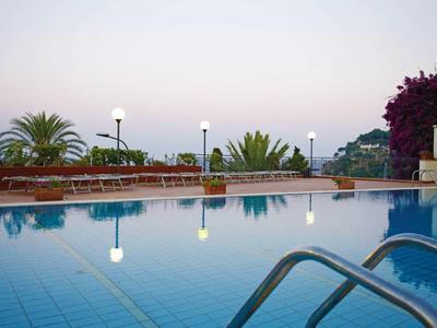 Zwembad met helder reflecterend water en palmbomen op de achtergrond bij zonsondergang.