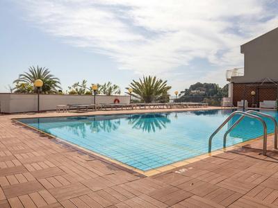 Buitenzwembad op terras met zonnescherm en palmbomen op de achtergrond onder een heldere lucht.