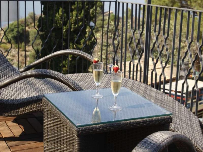 Balkon met rotan stoelen, glazen tafel en twee wijnglazen met uitzicht op zee.