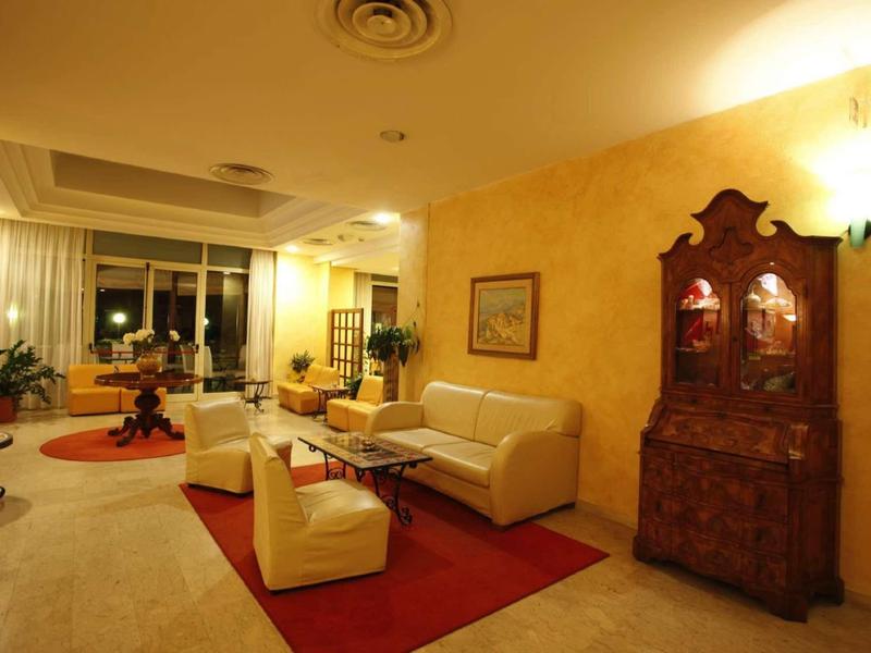 Gezellig hotel-loungegebied met banken, fauteuils en antieke kast tegen gele muur.