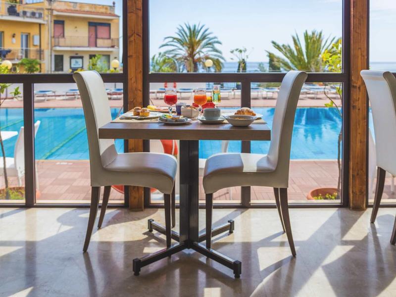 Eethoek met tafel en stoelen bij groot raam met uitzicht op het zwembad en palmbomen.