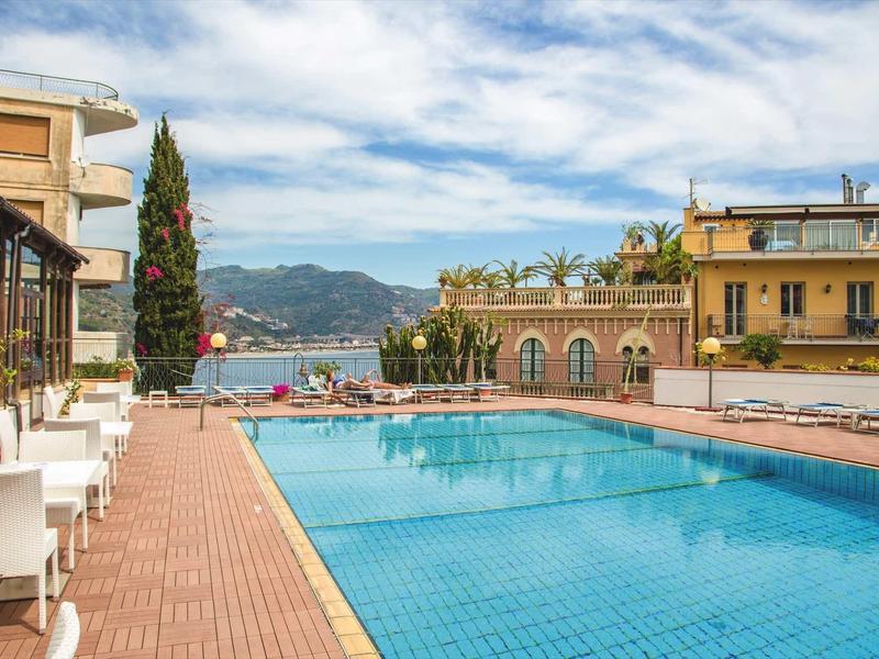 Buitenzwembad met uitzicht op zee en omliggende gebouwen onder een heldere lucht.