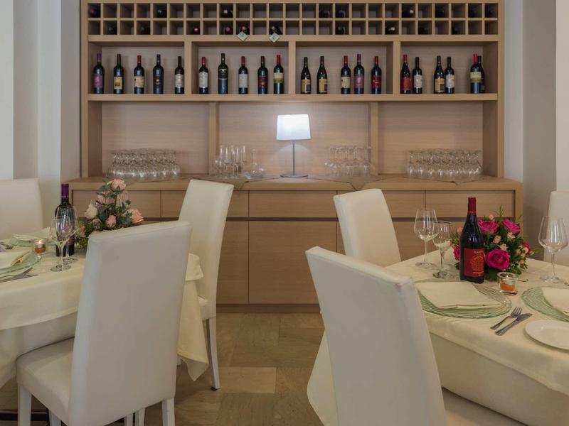 Elegant restaurant met witte stoelen, gedekte tafels en wijnrek aan de muur.