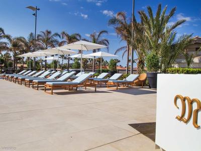 Rzędy leżaków z parasolami obok hotelowego basenu pod niebieskim niebem.