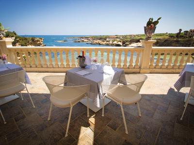 Taras z białymi krzesłami i stołami z widokiem na morze i linię brzegową.