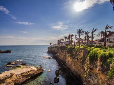 Falaise avec des palmiers et des maisons au bord de la mer sous un ciel bleu et le soleil.