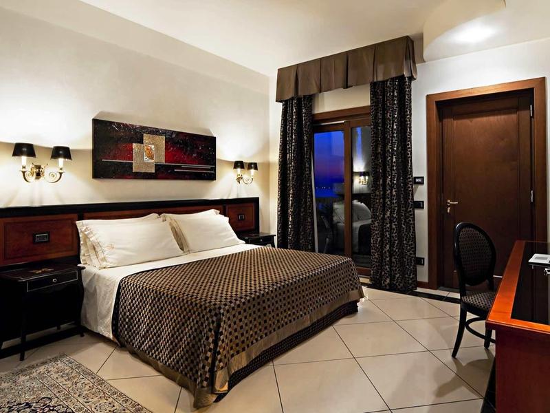 Przytulny pokój hotelowy z podwójnym łóżkiem, lampkami nocnymi i widokiem z okna o zmierzchu.