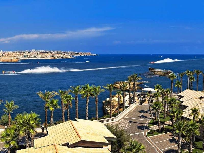 Panoramiczny widok nadmorskiego miasta z niebieskim morzem, palmami i budynkami pod czystym niebem.