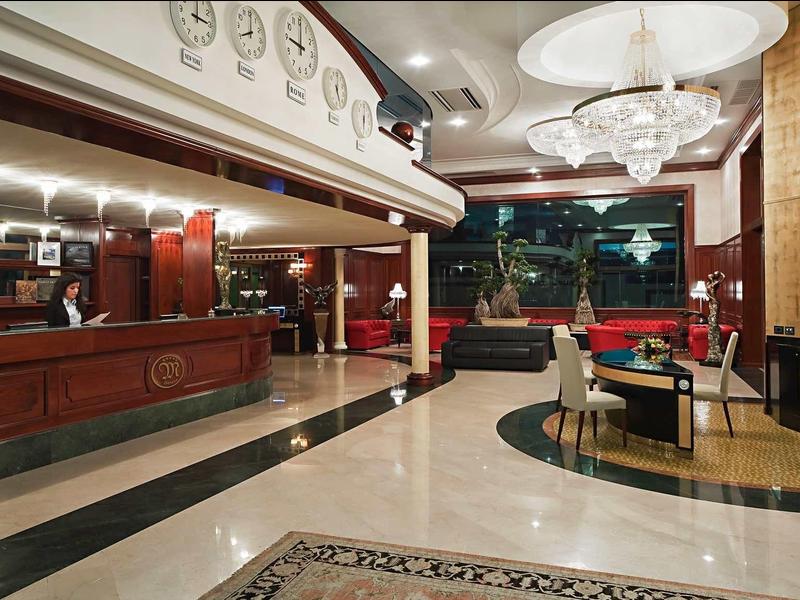 Przestronna lobby hotelowa z recepcją, marmurową podłogą i eleganckimi miejscami do siedzenia.