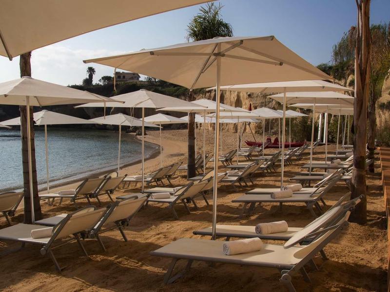 Plaża z leżakami i parasolami przy spokojnej wodzie i skalistym brzegu.