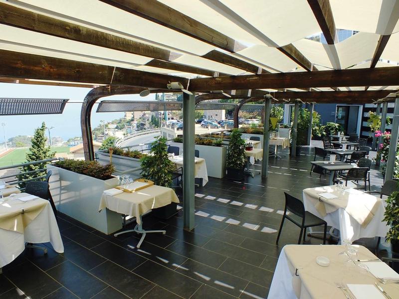 Overdekt buitenterras van een restaurant met tafels en stoelen, uitzicht op het water.