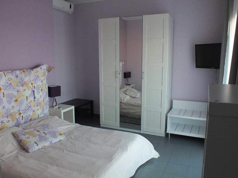 Slaapkamer met paarse muren, tweepersoonsbed, spiegelkast en airconditioning.