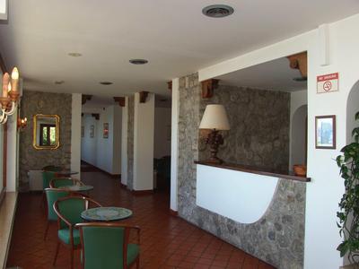 Hotel reception with stone wall, green upholstered chairs, and hallway with open doors.