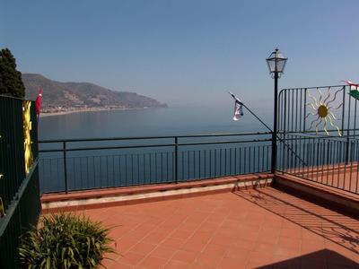 View over a terrace with the sea and mountains in the background under clear sky.