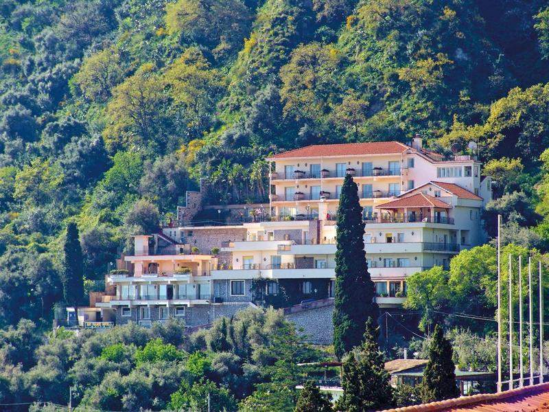 Multi-story hotel on a wooded hillside with Mediterranean vegetation.