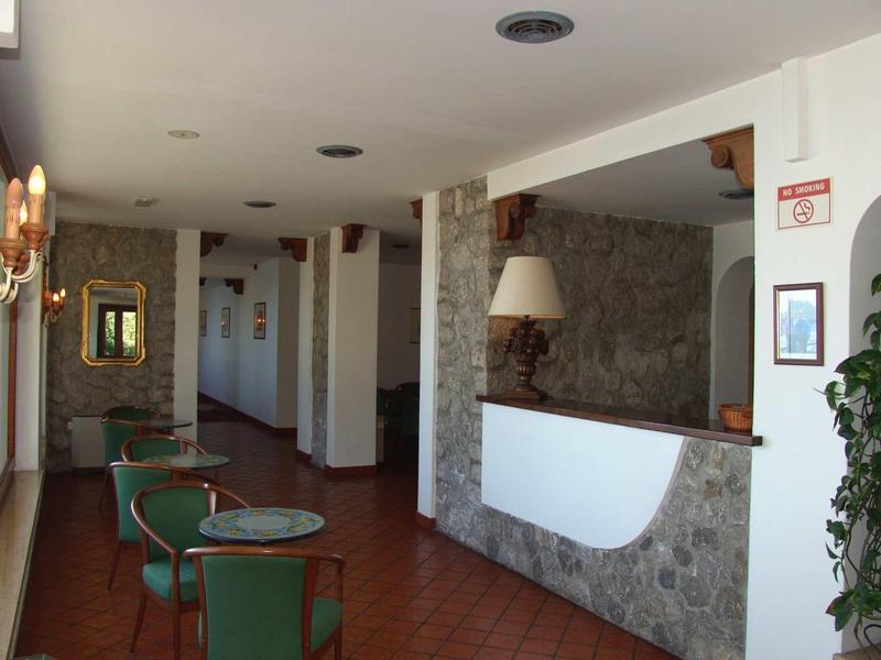 Hotel reception with stone wall, green upholstered chairs, and hallway with open doors.