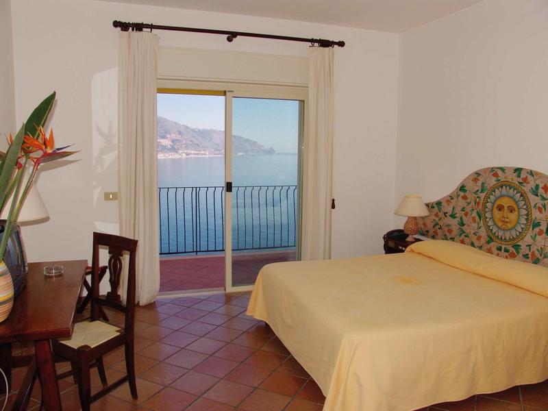 Bedroom with yellow bed, chair, desk, and sea view through a glass sliding door.