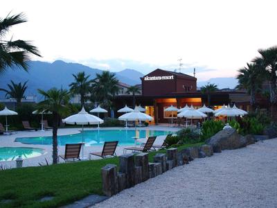 Vista serale di un hotel con piscina, sdraio e palme davanti alle montagne.