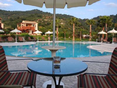Vista di una piscina rotonda con ombrelloni e colline sullo sfondo da una terrazza con tavolo e sedie.