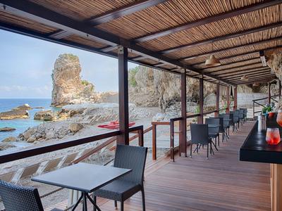 Terrazza aperta con sedie e tavoli con vista su rocce e mare.