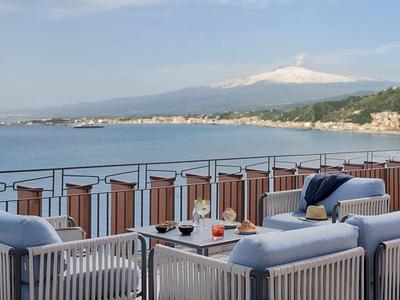 Terrazza con sedute e bevande vista mare e montagna innevata sullo sfondo.