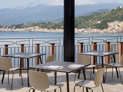 Vista di una terrazza con tavoli e sedie, mare e montagne sullo sfondo.