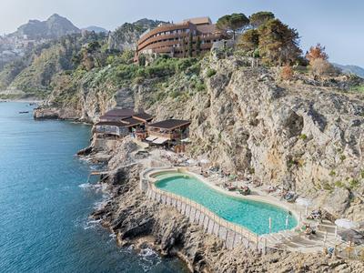 Hotel su una collina rocciosa con piscina che guarda il mare in condizioni di tempo sereno.