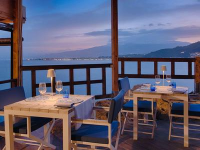 Terrazza con tavolo e sedie sul mare al tramonto con vista sulle montagne.