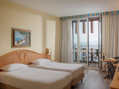 Camera d'hotel luminosa con due letti singoli, balcone e vista mare.