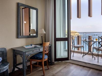 Camera d'hotel con scrivania, sedia e balcone con vista sul mare.