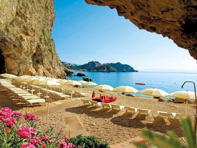 Strand met ligstoelen en bloemen, uitzicht vanuit een grot op zee en eilanden