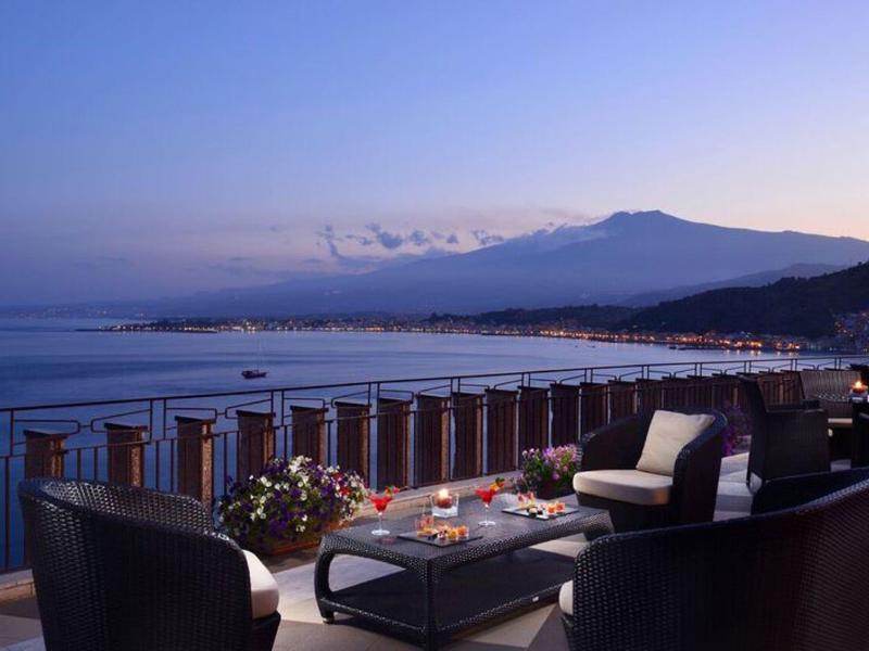 Balkon met zithoek met uitzicht op zee en bergen bij zonsondergang.