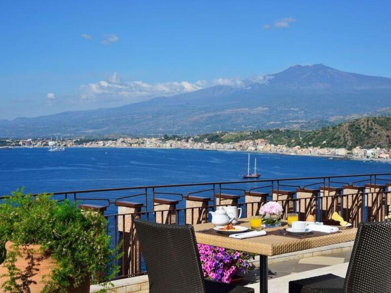 Terras met gedekte tafel met uitzicht op zee en bergen op de achtergrond.