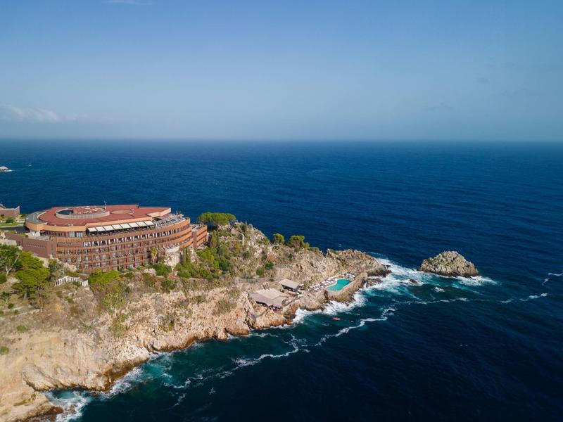 Hotel op rotsachtige kust met uitzicht op de blauwe zee en heldere lucht.