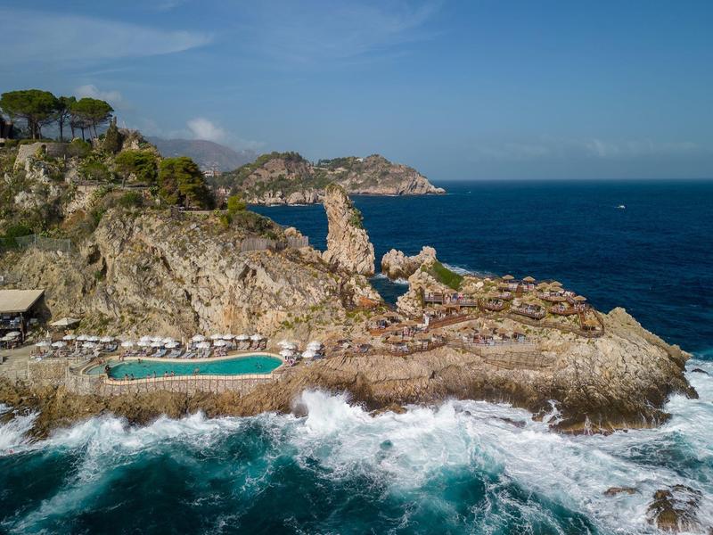 Rotsachtige kustlijn met een zwembad en uitzicht op de open zee bij heldere lucht.