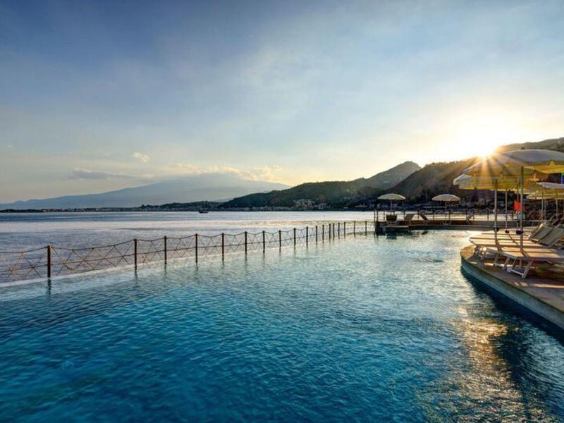 Infinityzwembad met uitzicht op zee en bergen bij zonsondergang.