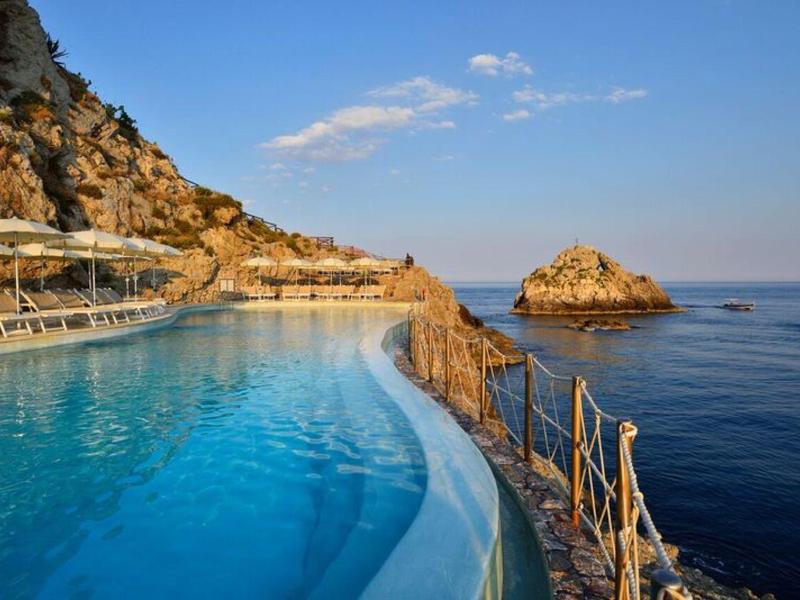 Infinity zwembad met uitzicht op de zee, omgeven door rotsen en een heldere lucht.