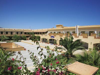 Hotel mit gelben Gebäuden, Pflanzen und klarem blauem Himmel im Hintergrund.