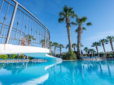 Piscina con acqua limpida e palme sotto un cielo azzurro in un resort alberghiero.