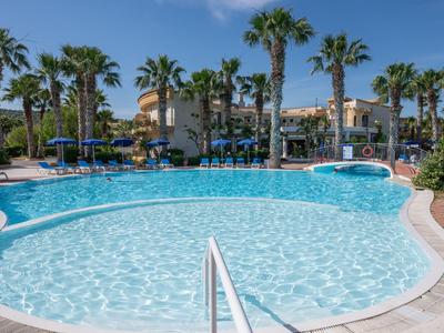 Grande piscina dell'hotel con palme e ombrelloni blu sotto un cielo limpido.