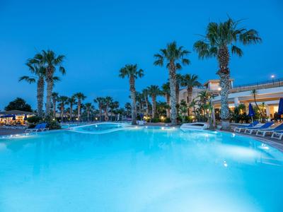 Una grande piscina dell'hotel al crepuscolo con palme e sdraio ai bordi.