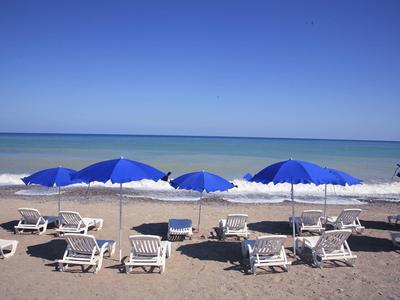 Beach with white loungers and blue umbrellas by calm sea under clear blue sky