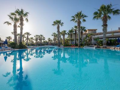 Großer klarer Pool mit Palmen und Liegestühlen in einer sonnigen Hotelanlage.