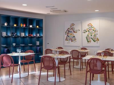 Moderner Essbereich mit runden Tischen, roten Stühlen und Kunst an den Wänden in einem Hotel.