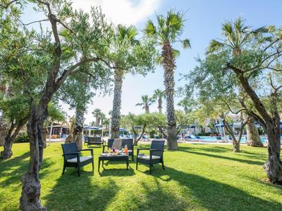 Grüner Garten mit Palmen und Stühlen auf Grasfläche in sonnigem Hotelbereich.