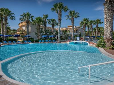 Großer Hotelpool umgeben von Palmen und Liegestühlen unter blauem Himmel.