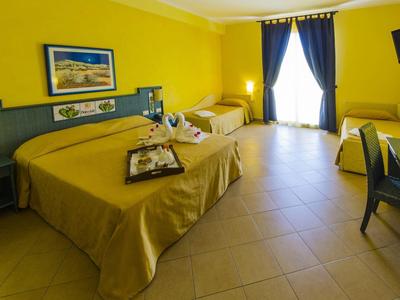 Bright hotel room with yellow walls, double bed, single bed, and wall-mounted TV.