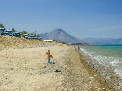 Beach with lounge chairs and umbrellas, mountain in the background, and blue sea under clear sky.