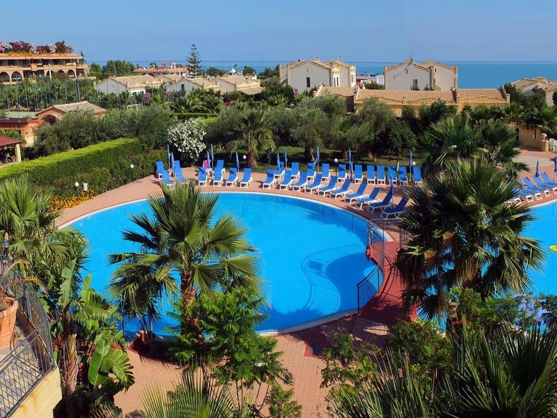 Hotel outdoor area with two large pools, palm trees, and lounge chairs under a blue sky.
